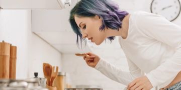 Frau kostet aus Topf am Herd