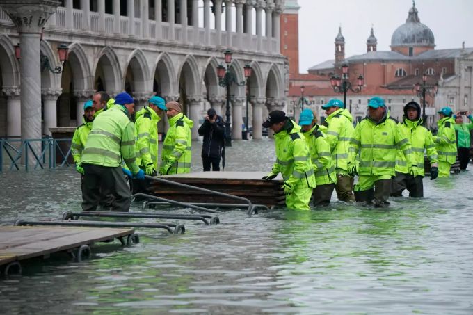 Männer installieren einen Holzsteg auf dem überfluteten Markusplatz. Überschwemmungen in Venedig