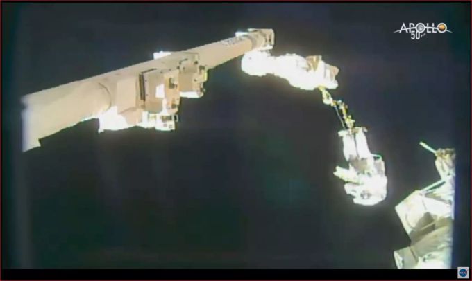 Ein Astronaut hängt bei einem Ausseneinsatz an der ISS an einem Roboterarm. Screenshot aus einem Livestream-Video der Nasa. Astronauten
