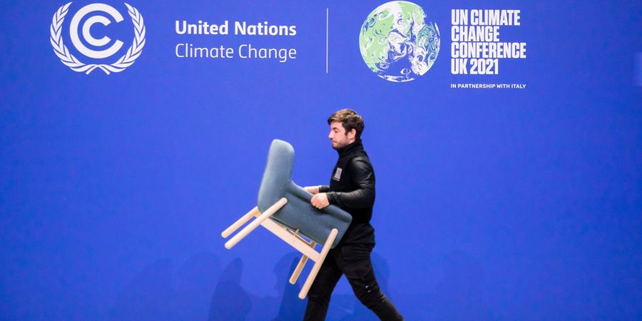 Ein Mitarbeiter trägt bei der UN-Klimakonferenz COP26 einen Stuhl von einer Bühne.