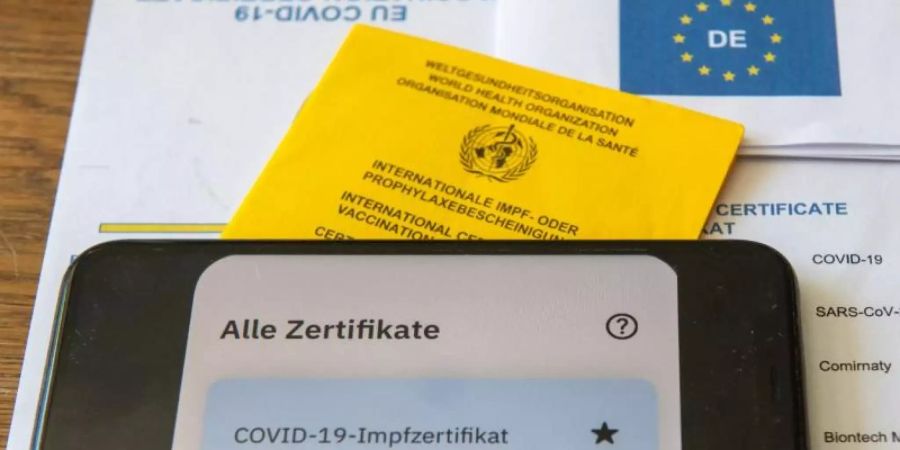 Ein Impfpass und ein Smartphone, auf dem die App CovPass läuft, liegen auf einem Impfzertifikat. Foto: Stefan Puchner/dpa