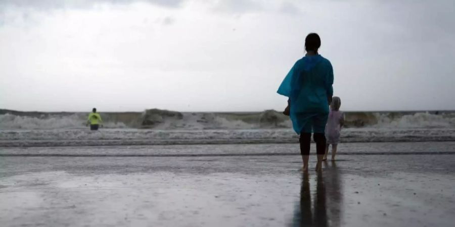 Kamila Struk (r) beobachtet ihren Vater Nickolas, der an einem gesperrten Strand in die Wellen watet, während der Tropensturm «Henri» über den US-Bundesstaat New York zieht. Foto: John Minchillo/AP/dpa