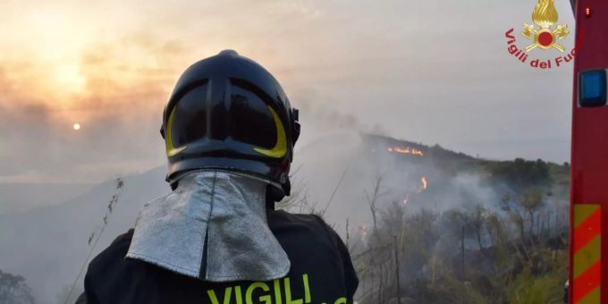 HANDOUT - 03.08.2021, Italien, ---: Ein Feuerwehrmann steht vor einem Gebiet, in dem mehrere Brände lodern (Aufnahmeort unbekannt). Waldbrände in Italien