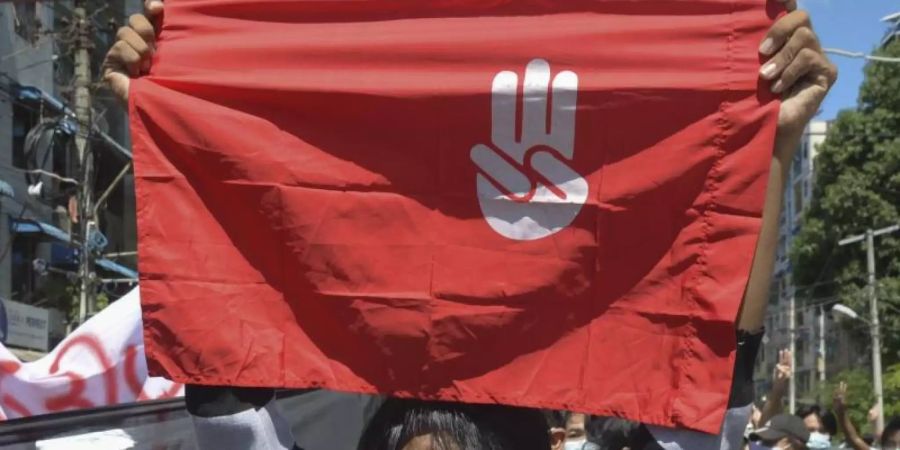 Ein Protestteilnehmer hält während einer Demonstration in Yangon eine Flagge hoch, auf der das Drei-Finger-Zeichen des Widerstandes zu sehen ist. Foto: Uncredited/AP/dpa