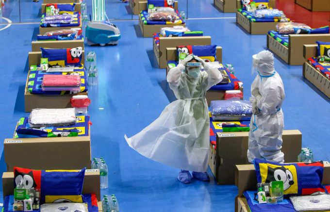 Mitarbeiter des Gesundheitswesens in Schutzkleidung stehen zwischen Betten, die für Corona-Patienten vorbereitet wurden in einer provisorischen Krankenstation im Nimibutr-Stadion. Coronavirus - Thailand