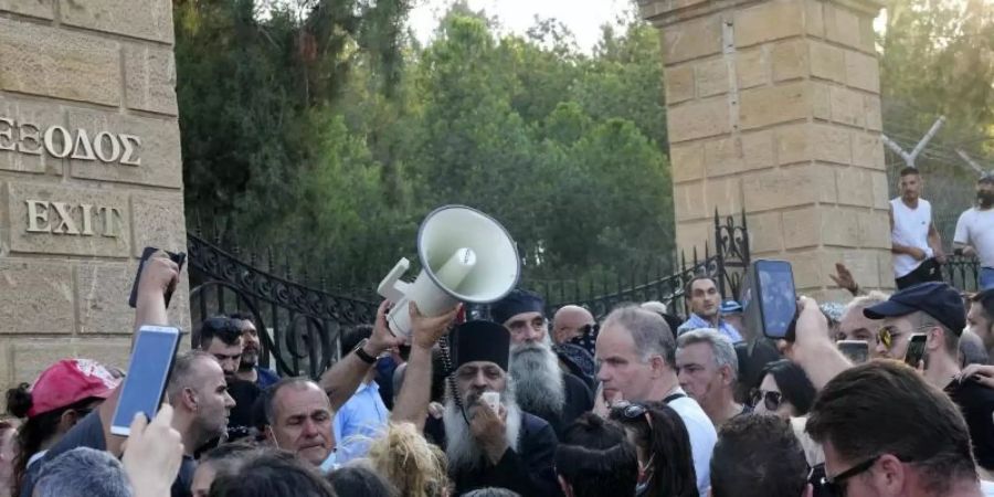 Ein griechisch-orthodoxer Priester spricht zu Demonstranten während des Protests gegen die Corona-Massnahmen vor dem Präsidentenpalast. Foto: Petros Karadjias/AP/dpa