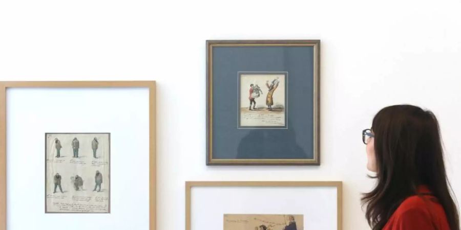 Eine Zeichenserie von Graf von Pocci (1850) schaut sich in der Ausstellung "Unveröffentlicht - Die Comicszene packt aus" eine Fachbesucherin an. Foto: Roland Weihrauch/dpa