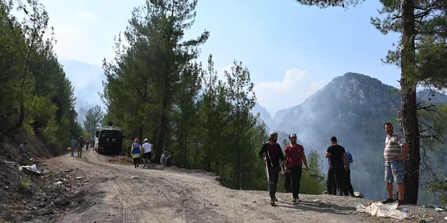 Helfer stehen an einem Waldweg während im Hintergrund Qualm über der Landschaft der Gemeinde im westtürkischen Mugla aufsteigt.