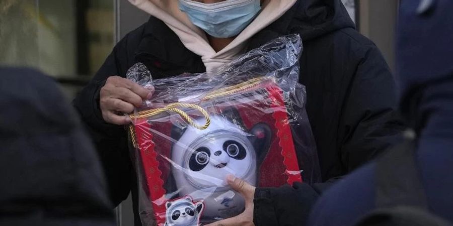 Ein Mann hält die Puppe des olympischen Maskottchens Bing Dwen Dwen in der Hand, die er in einem Geschäft in Peking gekauft hat. Foto: Andy Wong/AP/dpa