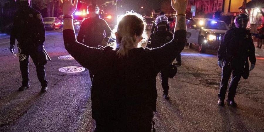 Eine Demonstrantin steht bei einem Protest gegen Polizeigewalt in Oakland mit hochgestreckten Armen vor Polizisten. Foto: Ethan Swope/AP/dpa