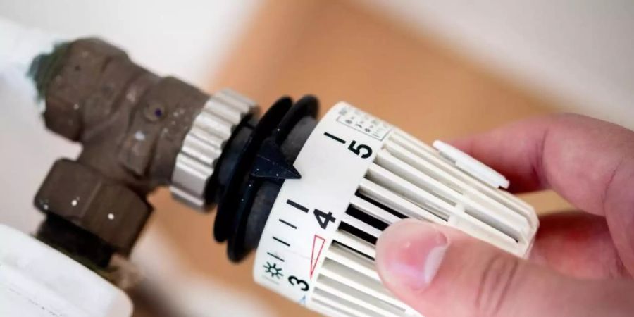 Ein Mann dreht in einer Wohnung am Thermostat einer Heizung. Foto: Hauke-Christian Dittrich/dpa