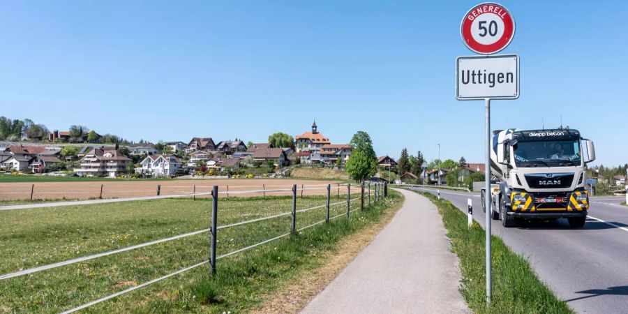 Ortsschild Uttigen mit Blick auf das alte Schulhaus.