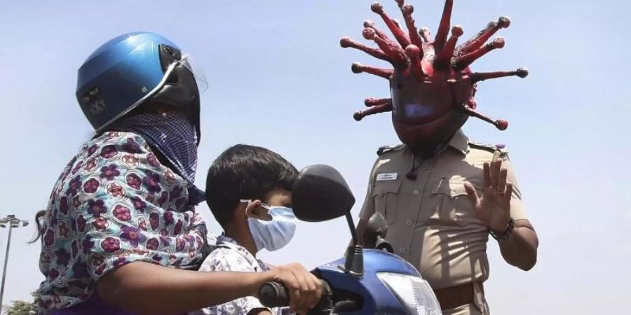 Ein Polizeibeamter im indischen Chennai trägt einen Helm, der einem Virus ähnelt, und weist Pendler auf die Einhaltung der Ausgangsbeschränkungen hin. Foto: R. Parthibhan/STR/AP/dpa