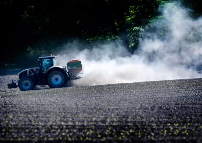 Ein Traktor düngt ein Feld und zieht eine Staubwolke hinter sich her. Agrarpolitik 2022+