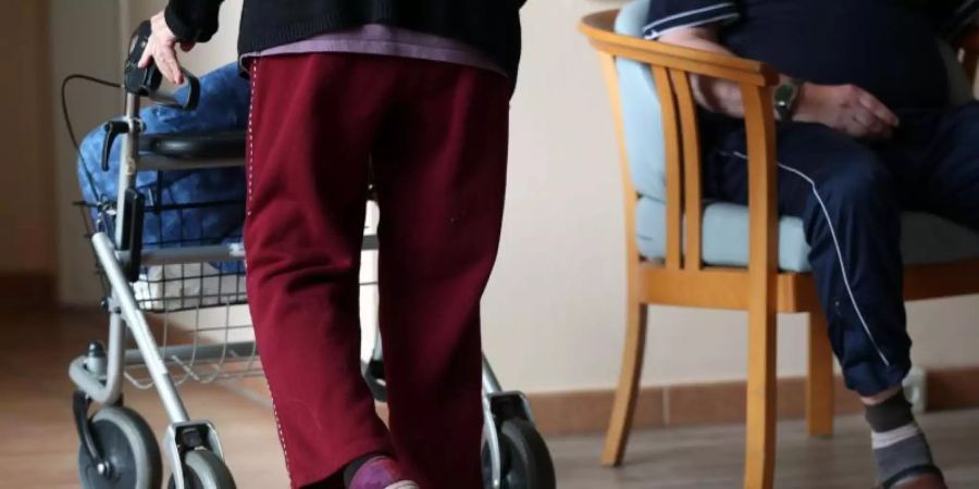 Eine ältere Frau geht mit einem Rollator über einen Flur eines Pflegeheims. Foto: Jens Büttner/zb/dpa