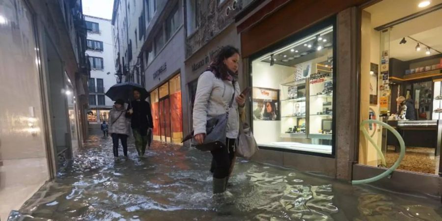 Menschen waten in Gummistiefeln durch Hochwasser in einer Gasse in Venedig. Foto: Andrea Merola/ANSA/AP/dpa