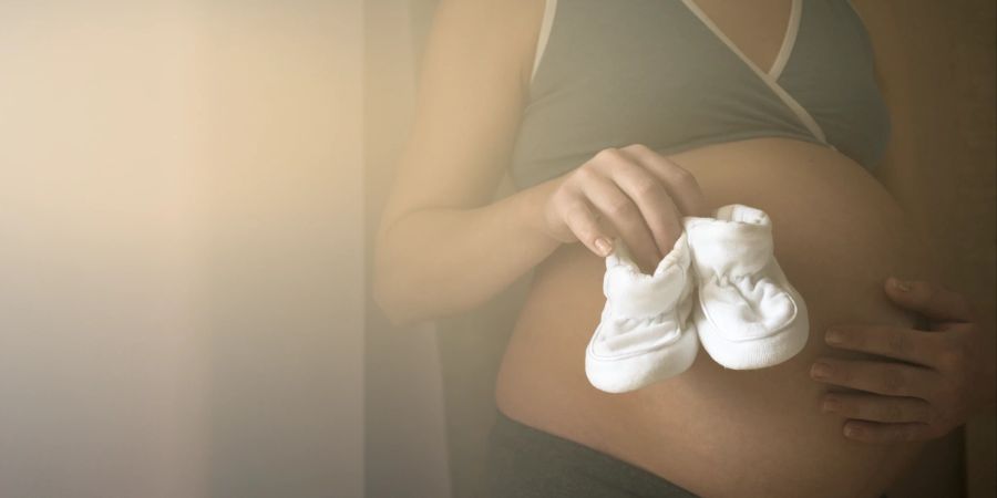 schwangere frau hält babyschuhe