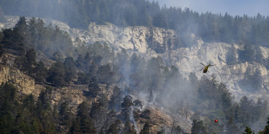 Ein Helikopter wirft Wasser auf das Feuer in Bitsch VS.