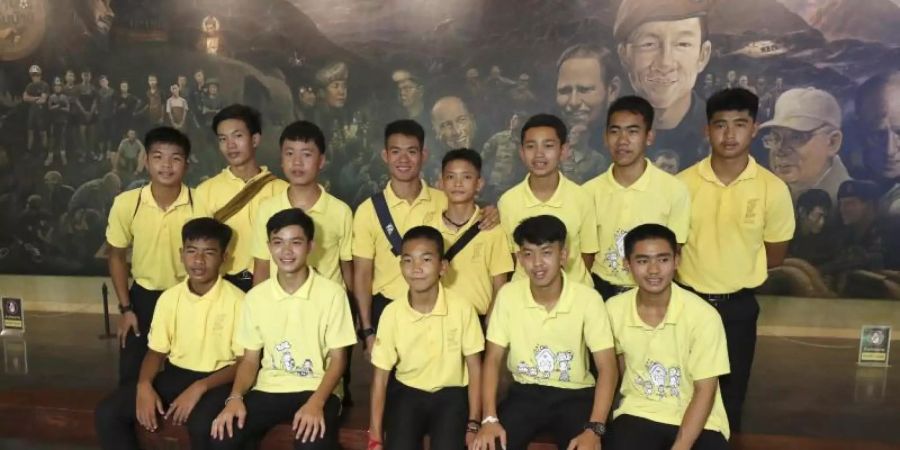 Die 12 Jungs der Fussballmannschaft der «Wildschweine» aus Mae Sai und ihr ehemalige Fussballtrainer Ekkapol Chanthawong (4.v.l, hintere Reihe), die zusammen vor drei Jahren aus der überfluteten Tham-Luang-Höhle gerettet wurden, bei einer Pressekonferenz. Foto: Sakchai Lalit/AP/dpa