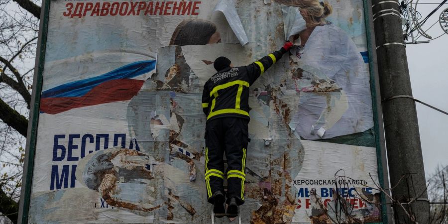 Ein ukrainischer Feuerwehrmann reisst in der kürzlich befreiten Stadt Cherson eine russisches Werbeplakat von einer Werbetafel.