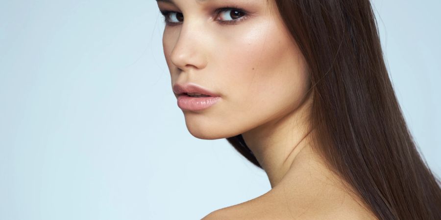 Model mit zartem Nude-Make-up und langen glatten braunen Haaren ohne Top.