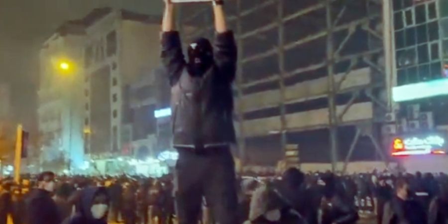 SCREENSHOT - In diesem Bild aus einem Video, das die Nachrichtenagentur AP außerhalb des Irans erhalten hat, hält ein maskierter Demonstrant ein Bild des iranischen Kronprinzen Reza P...