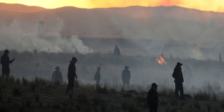 dpatopbilder - In der Nähe von El Alto in Bolivien stehen regierungskritische Demonstranten auf einem Feld inmitten von Tränengaswolken der Polizei. Foto: Juan Karita/AP/dpa