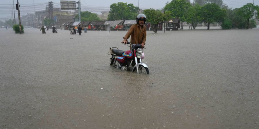 Ein Mann schiebt sein Motorrad über eine von heftigen Monsunregenfällen überflutete Straße. Foto: K.M. Chaudary/AP/dpa