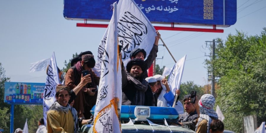ARCHIV - Anhänger der Taliban-Regierung fahren auf einem Fahrzeug mit, schwenken Taliban-Fahnen und machen Fotos während der Feierlichkeiten zum fünften Jahrestag des US-Abzugs aus A...