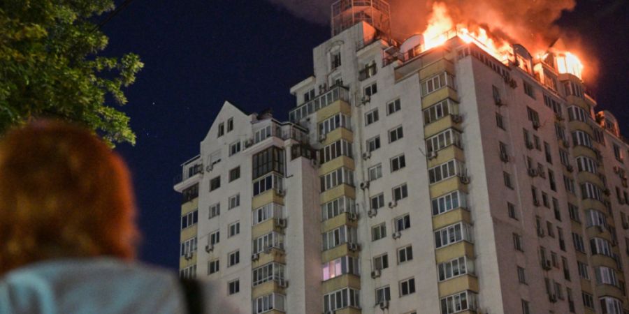 Eine Frau blickt auf ein Wohnhaus, das nach einem russischen Raketenangriff in Flammen steht. Foto: Danylo Antoniuk/AP/dpa