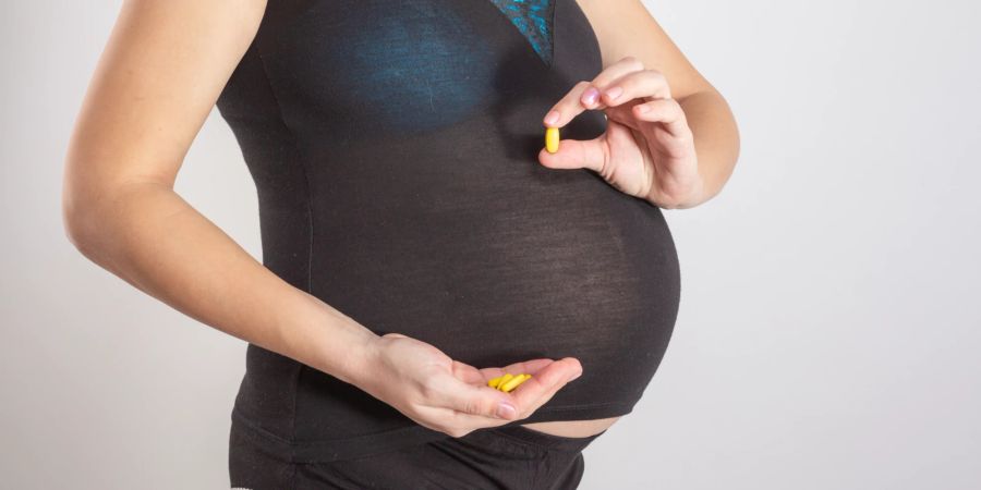 Schwangere Frau mit Nahrungsergänzungsmitteln in der Hand.