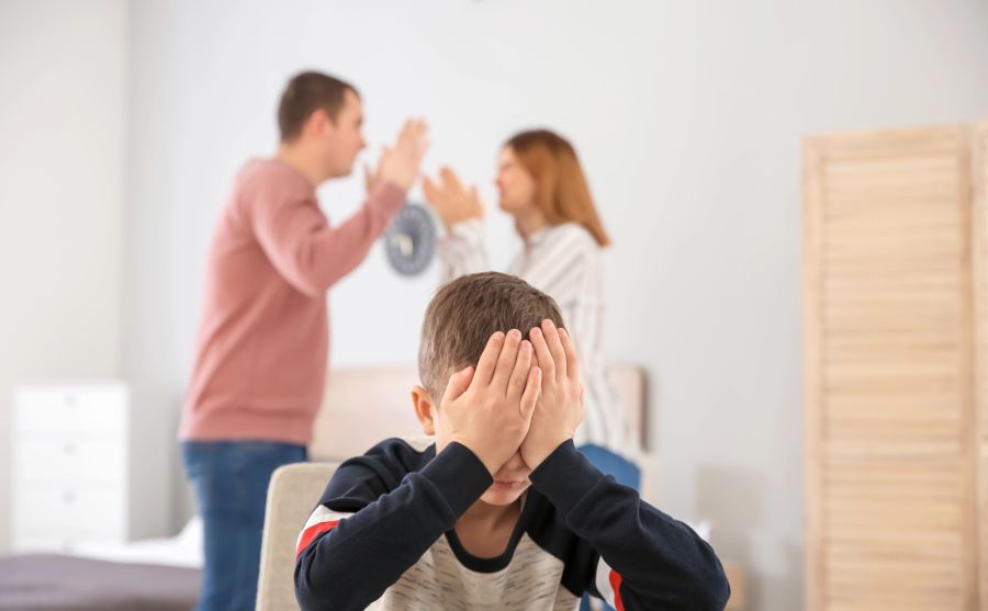 Kind hält sich Augen zu, Eltern streiten im Hintergrund