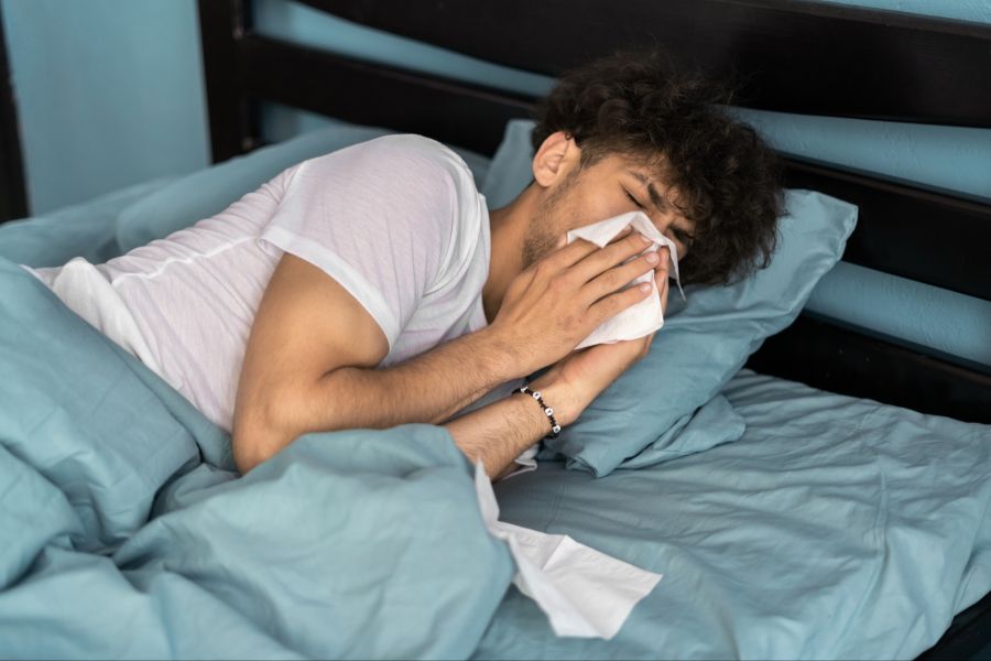 Kranker Mann im Bett putzt sich die Nase