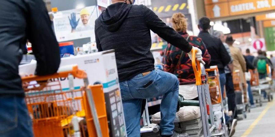 Kunden stehen mit Einkaufswagen in einem Baumarkt in einer Schlange vor den Kassen an. Die globalen Verwerfungen in den Lieferketten setzen Deutschlands Bau- und Gartenmärkte unter Druck. Foto: Sven Hoppe/dpa