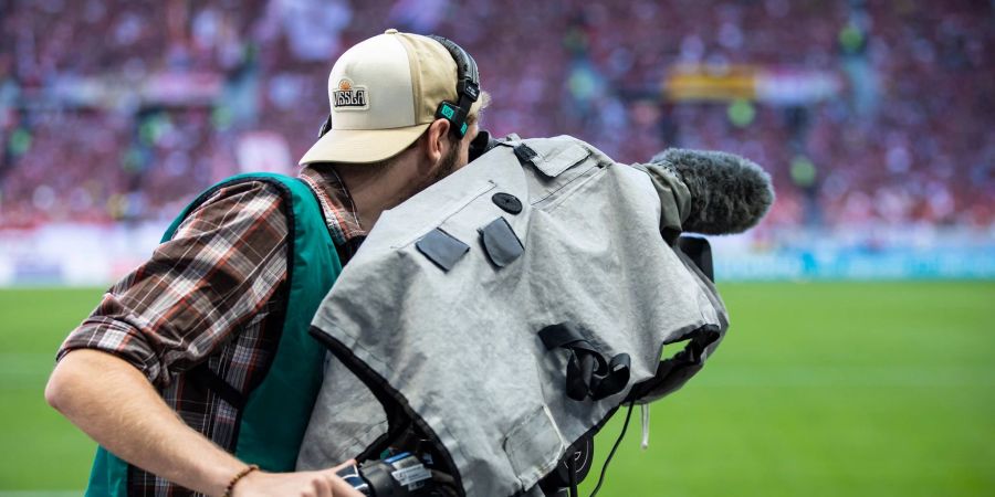 Ein Kameramann steht am Spielfeldrand und filmt ein Fussballspiel.