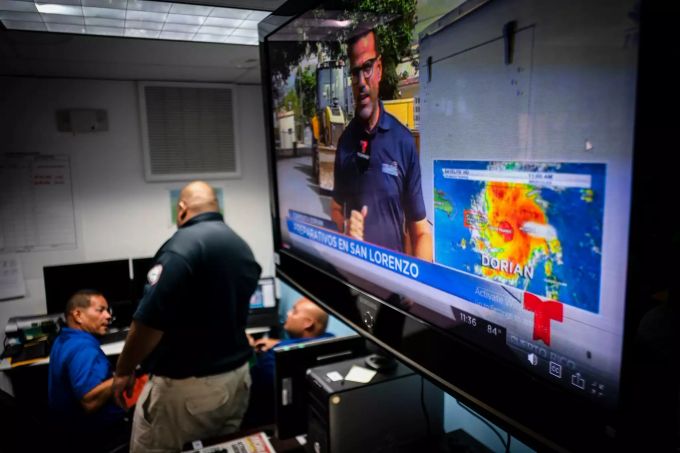Wettervorhersage Corona Krise: Das Personal des Notzentrums steht neben einem Fernseher, der ein meteorologisches Bild des Tropensturms «Dorian» zeigt. Foto: Ramon Espinosa (Archivbild) Wettervorhersage Corona Krise