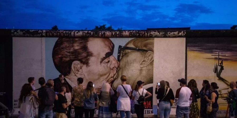 Touristen und Besucher stehen vor dem sogenannten «Bruderkussgemälde» an der East Side Gallery. Vor fast 30 Jahren hatten sich hier Künstler verewigt und das längste noch erhaltene Teilstück der Berliner Mauer mit ihren Kunstwerken umgedeutet. Foto: Arne Immanuel Bänsch