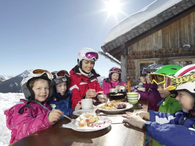 Eine Skilehrerin mit Kindern beim Mittagessen auf einer Hütte beim Kinderskikurs in Schladming (A). skischullehrer