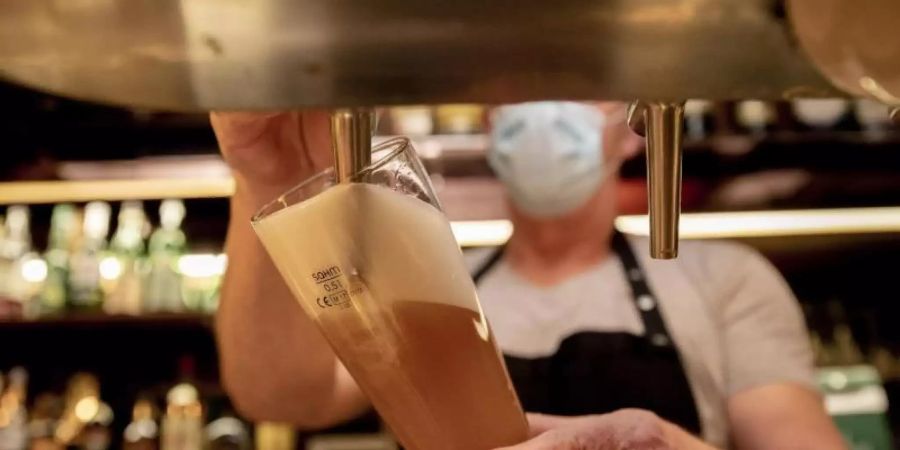 Ein Wirt mit Maske zapft in einer Kneipe im Berliner Bezirk Wilmersdorf ein Bier. Die Sperrfrist in der Bundeshauptstadt ist vor Gericht gekippt worden. Foto: Christoph Soeder/dpa