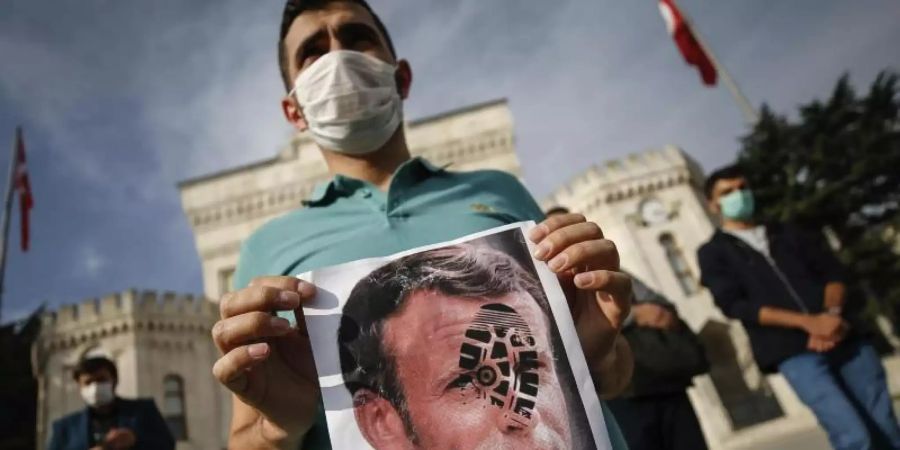 Ein junger Mann hält in Istanbul ein mit einem Schuhabdruck versehenes Foto von Emmanuel Macron in die Kamera. Foto: Emrah Gurel/AP/dpa