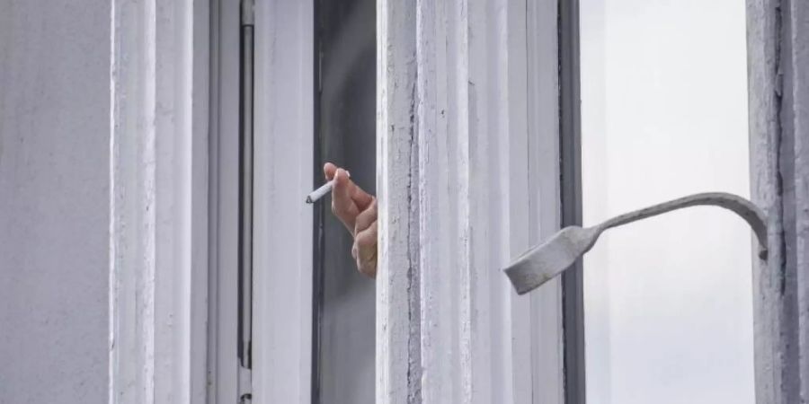 Ein Mann raucht während der Ausgangsbeschränkung am Fenster. Foto: Frank Rumpenhorst/dpa