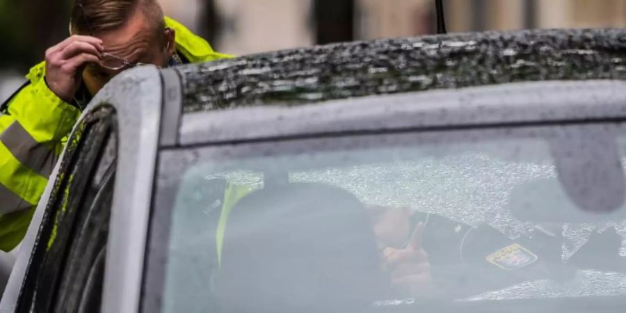 Zwei Polizeibeamte begutachten ein Fahrzeug mit beschädigter Heckscheibe im abgesperrten Bereich. In der Innenstadt von Rüsselsheim kam es zu Schüssen. Foto: Andreas Arnold
