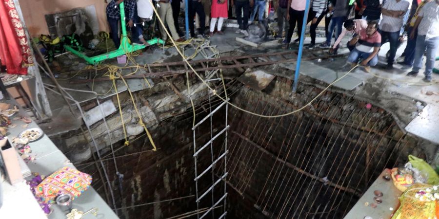 Menschen stehen an einem alten Brunnenbauwerk, über dem ein Tempel gebaut worden war, dessen Boden eingestürzt ist.