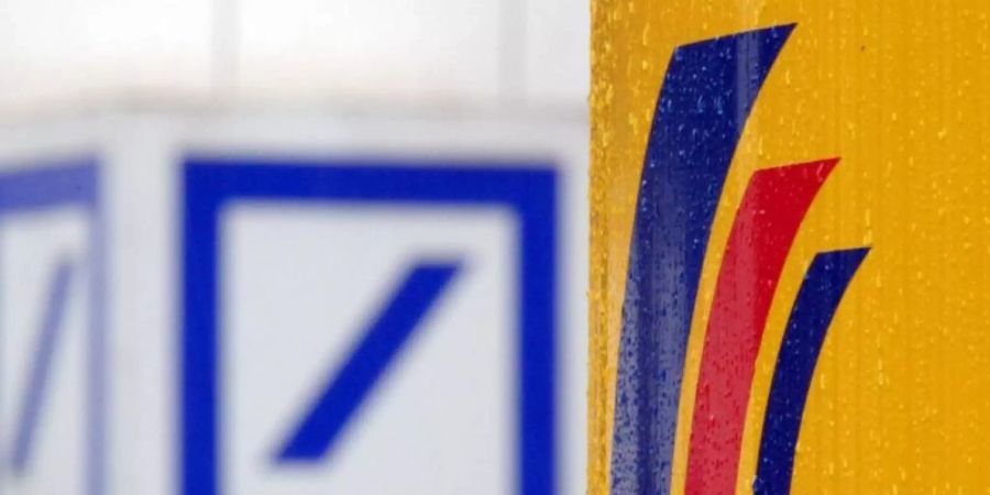 Das Logo einer Filiale der Deutschen Bank (l) und das Logo der auf der gegenüberliegenden Strassenseite befindlichen Postbank-Zentrale. Foto: Federico Gambarini/dpa