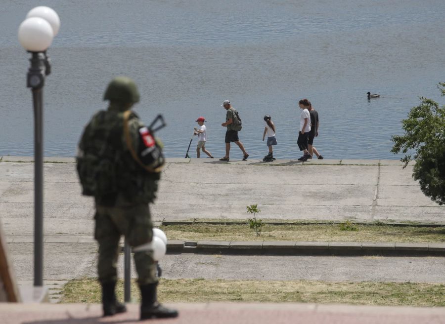 Ein russischer Soldat beobachtet eine Familie im Ukraine-Krieg, die am Fluss Dnepr in Kherson entlang spaziert.