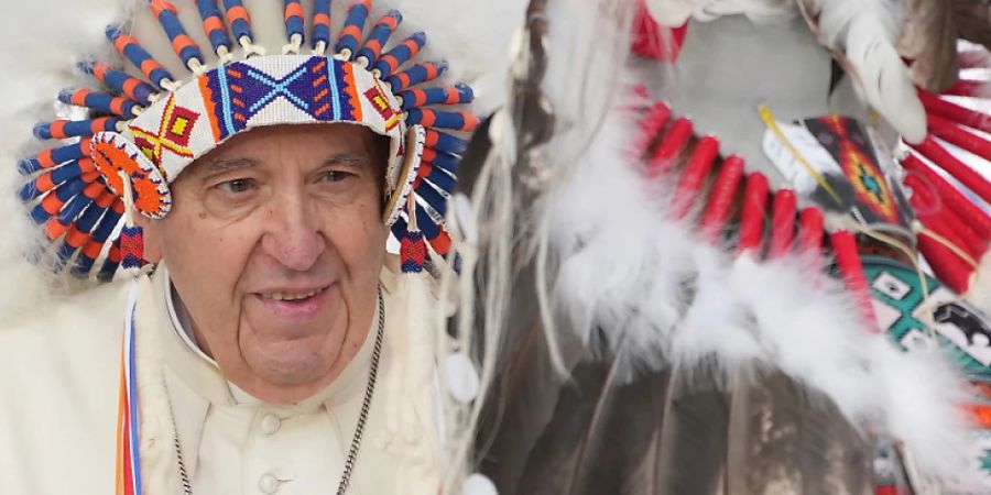 Papst Franziskus (l) trägt einen indigenen Kopfschmuck während eines Treffens mit indigenen Gemeinschaften, darunter Vertreter der First Nations, Métis und Inuit, in der katholischen Kirche Our Lady of Seven Sorrows. Papst Franziskus hat die Ureinwohner Kanadas um Vergebung für die einst von Kirchenvertretern begangenen Vergehen an indigenen Kindern gebeten. Foto: Nathan Denette/The Canadian Press via AP/dpa