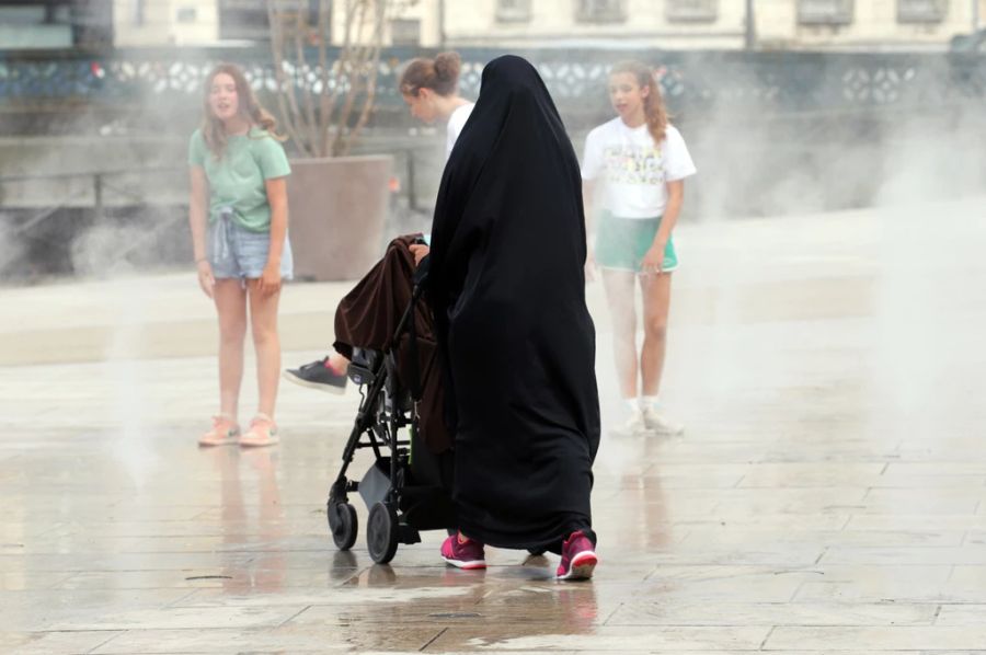 Bei diesem Wetter nicht zu beneiden: Eine Frau mit Burka gönnt ihrem kleinen Kind eine Abkühlung mit einer Fahrt durch einen Brunnen in Bayonne.