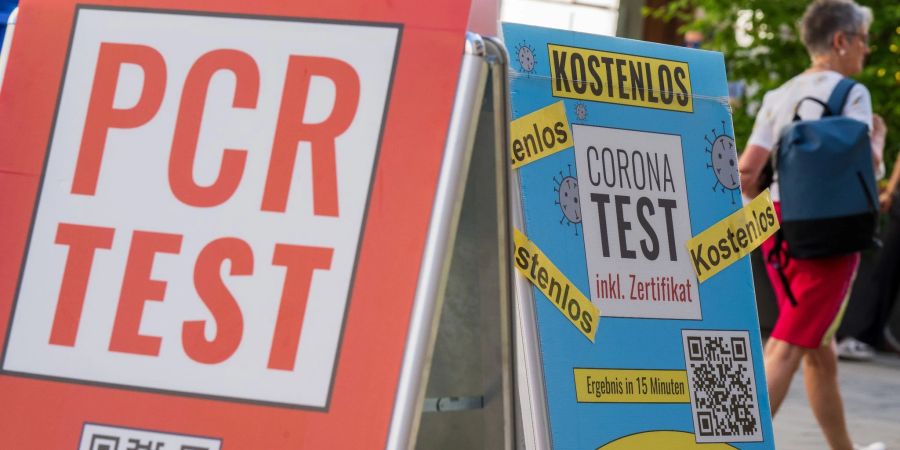 Schilder mit der Aufschrift «PCR Test» und «Corona-Test - Kostenlos» hängen vor dem Eingang einer Apotheke in der Innenstadt von München.