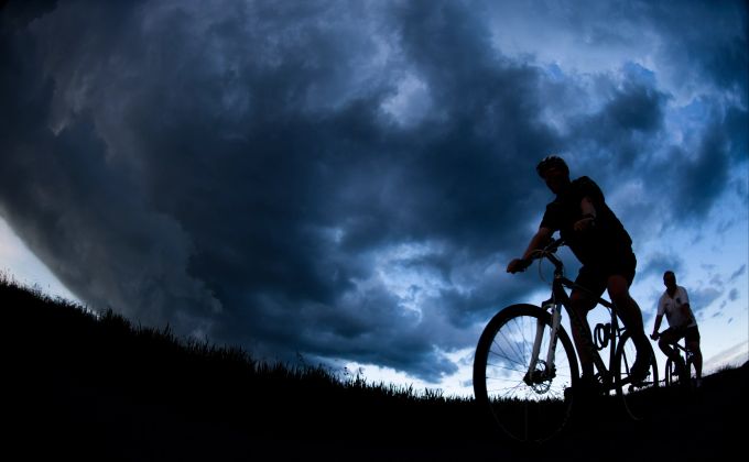 Schnell weg! Bei einem Gewitter muss man sich entweder in einem Gebäude in Sicherheit bringen – oder vom Velo absteigen und Schutz in einer Mulde suchen. Himmel Gewitter Velofahrende Gras