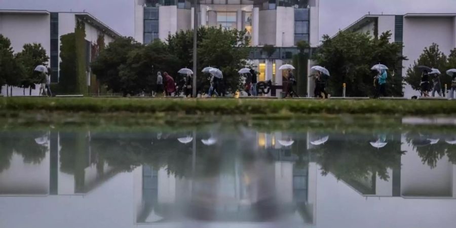 Kühl und grau: Eine Gruppe mit Regenschirmen geht am Bundeskanzleramt vorbei. Foto: Christoph Soeder